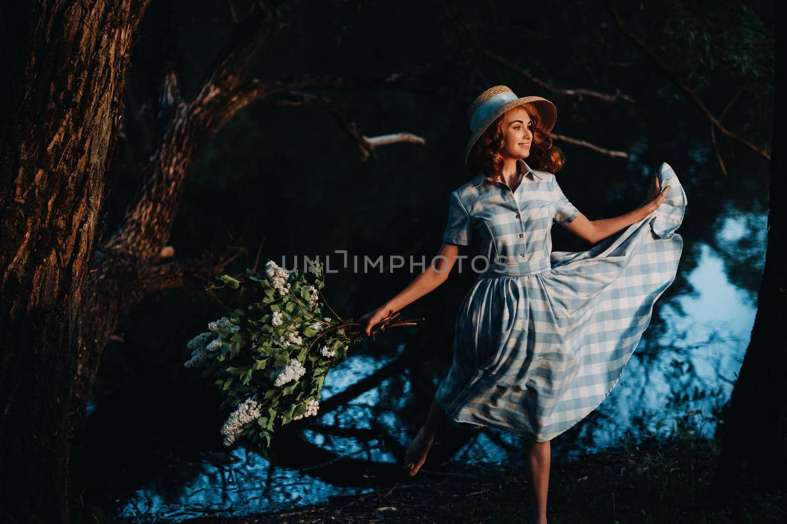 Portrait of a beautiful girl with long hair, a straw hat and a long summer dress with lilac flowers in the garden.