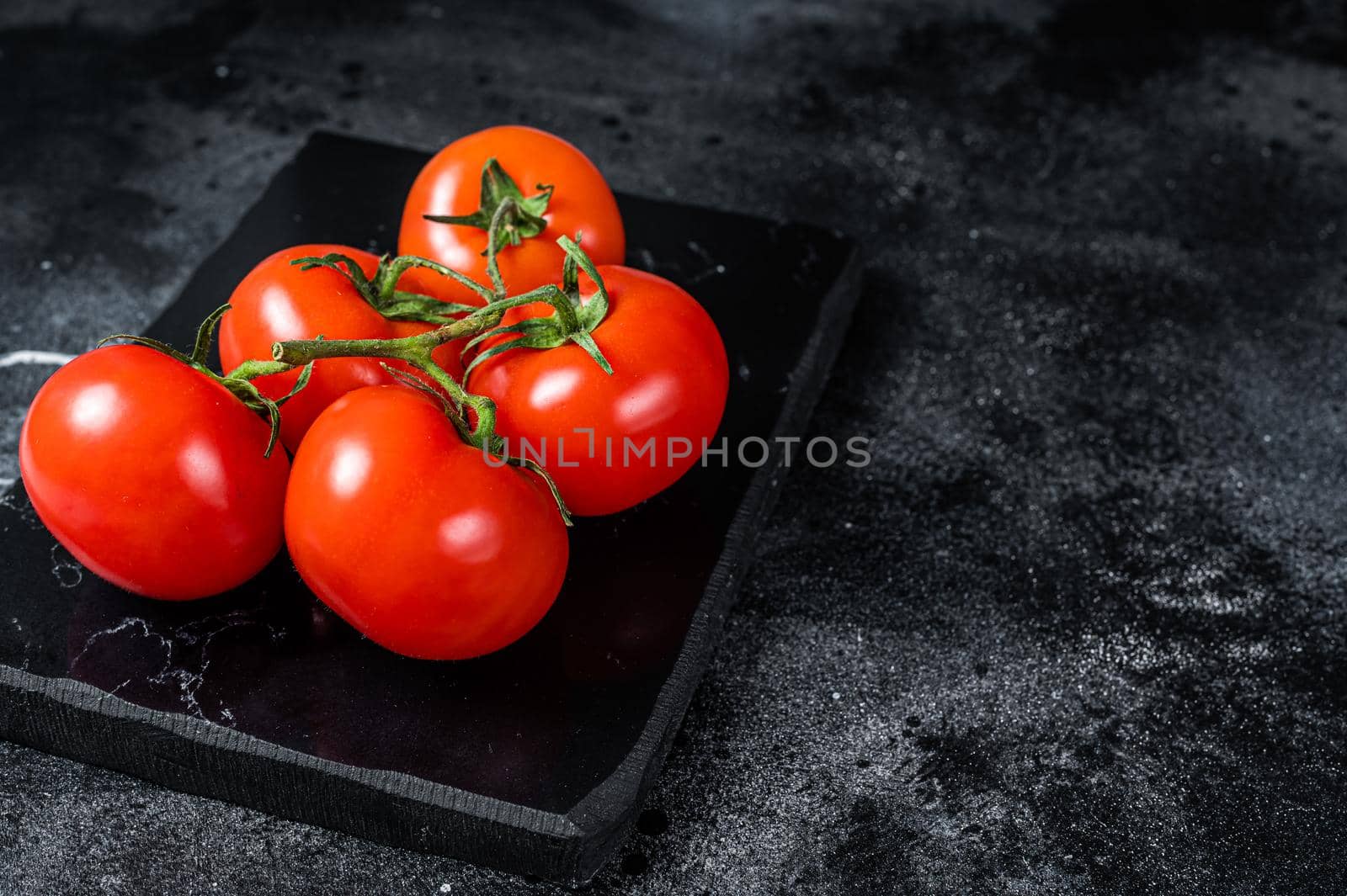 Branch of Red cherry tomatoes on marble board. Black background. Top view. Copy space.