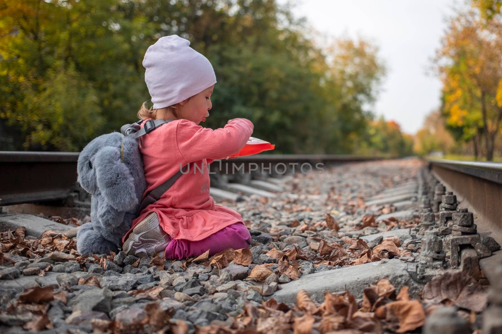 danger games. cute little toddler girl playing outdoors witch stone on the railway tracks.