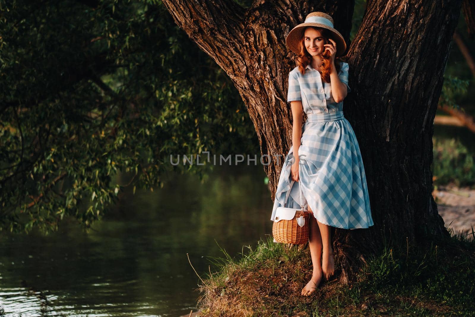 a young beautiful girl in a straw hat and with a straw bag enjoys the view of the lake.
