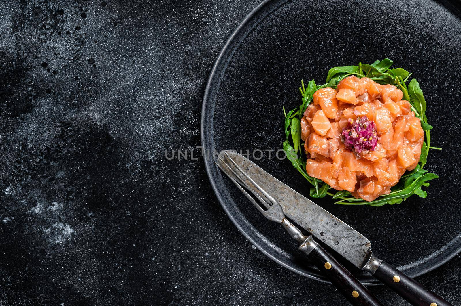 Raw Salmon tartare or tartar with red onion, arugula and capers in black plate. Black background. Top View. Copy space.