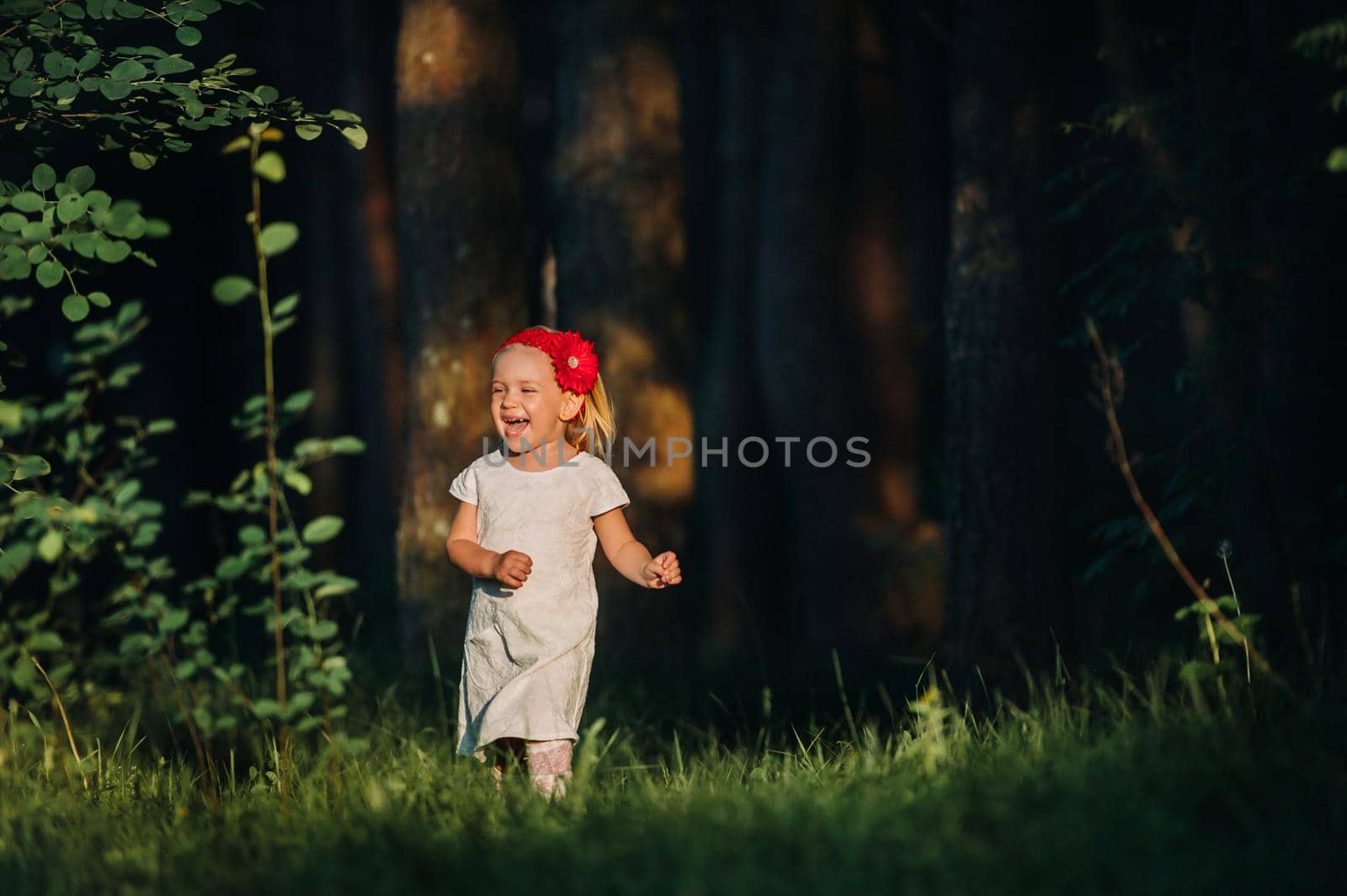 Portrait of a cute little girl runs on a green lawn in a forest. A happy child laughs and smiles. Sunny forest, a ray of sunshine