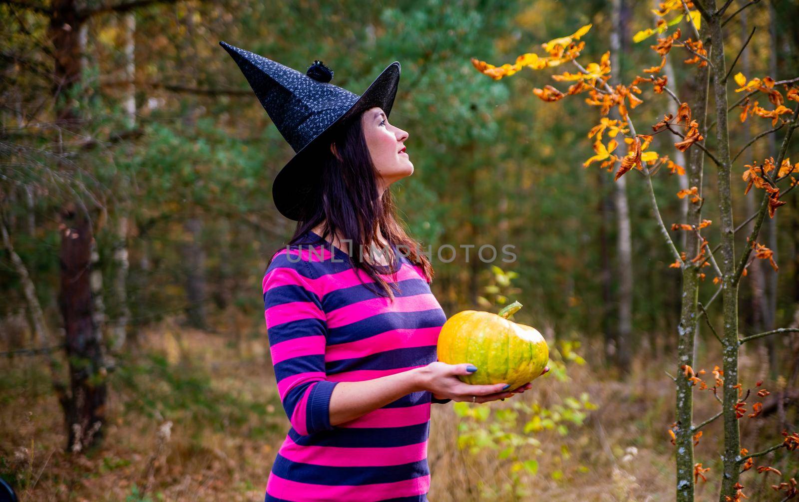 Witch with little pumpkin in autumn forest by Mariaprovector