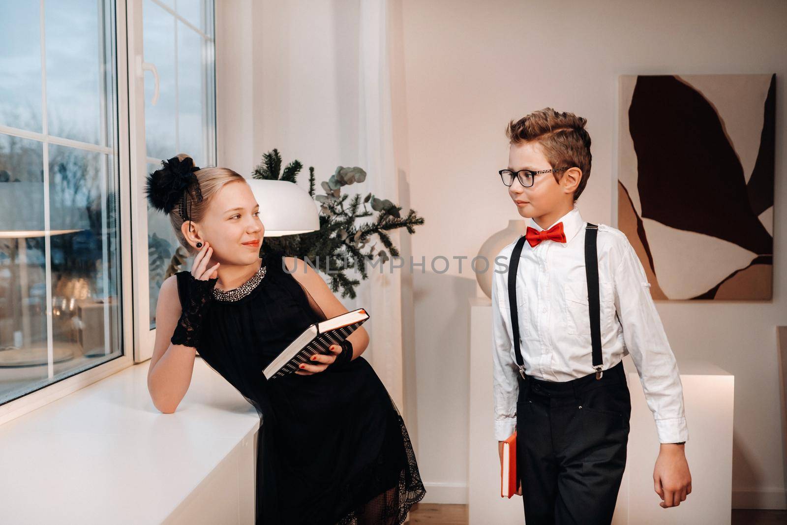Stylish boy and girl stand near the window with books in their hands.