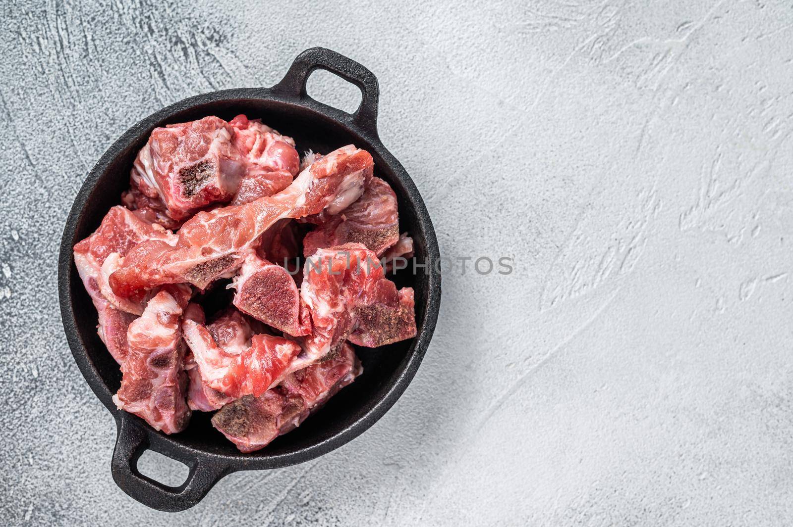 Raw diced meat cubes with bone in a pan. White background. Top View. Copy space by Composter
