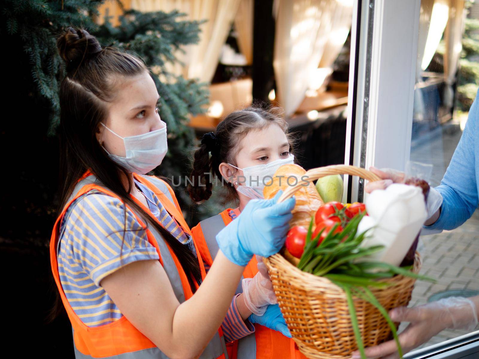 Teen girls in protective masks deliver a basket of food during the quarantine, the people who are on isolation. by Utlanov