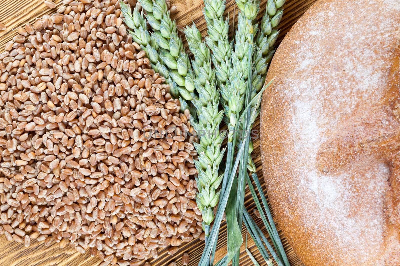wheat grains, green wheat ears and bread lying on a wooden table, close-up photo from above