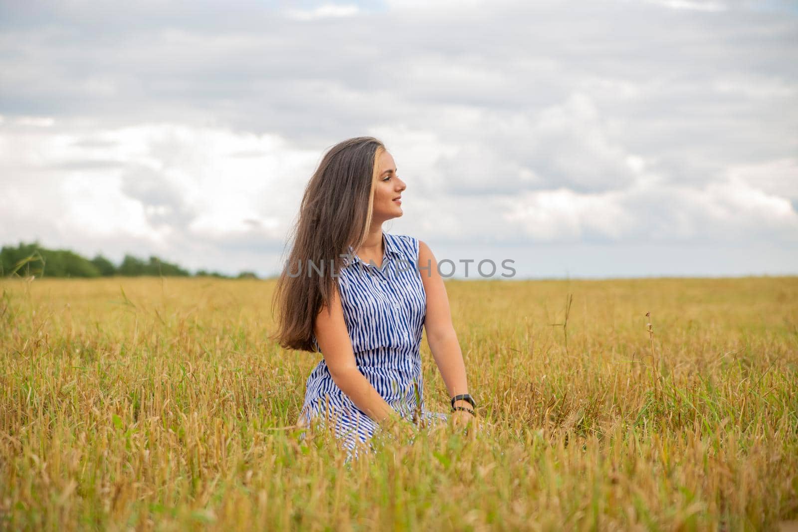 beautiful swarthy young woman sits in a meadow on a sunny day and enjoys the summer weather and wind.