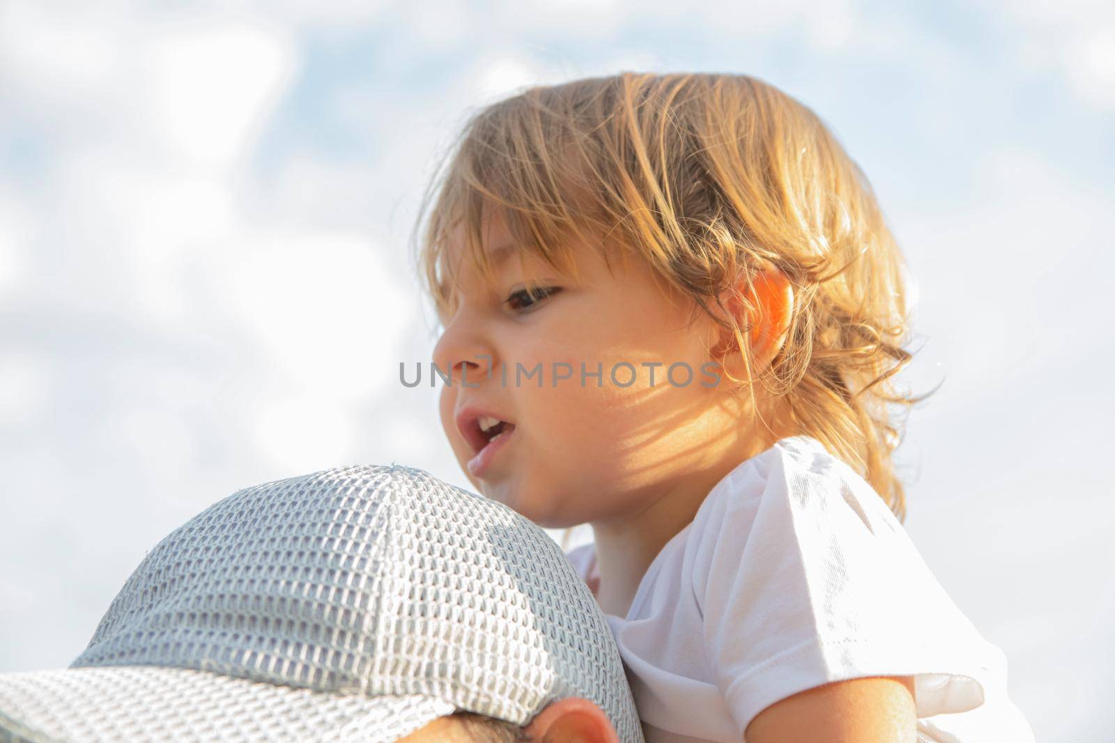 adorable toddler sits on dad's shoulders close-up. portrait of a child sitting on the father's neck. happy family
