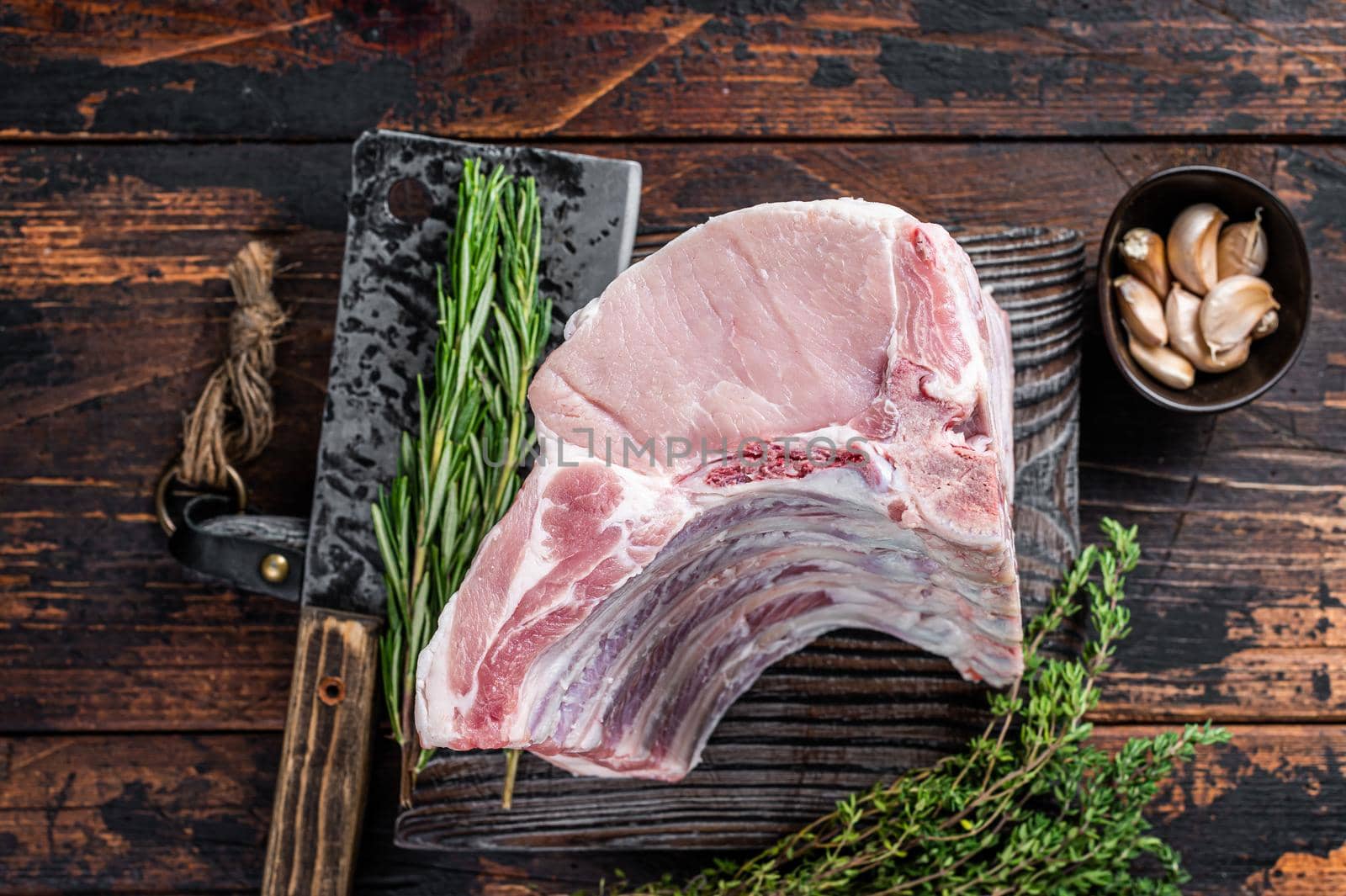 Raw rack of pork loin chops with ribs on a butcher board with meat cleaver. Dark wooden background. Top view.