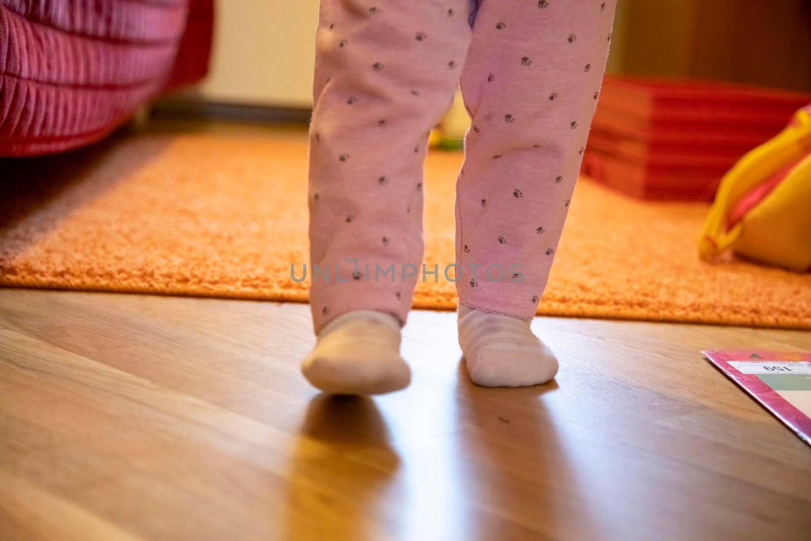 the legs of a small child are walking around the room. baby's first steps concept. no face by Mariaprovector