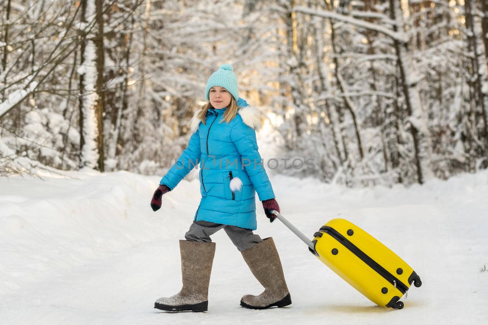 A girl in winter in felt boots goes with a suitcase on a frosty snowy day.