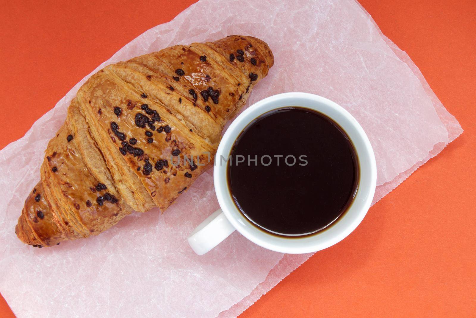 Black coffee without milk in a white cup and a chocolate croissant on parchment and bright background. French breakfast with fresh pastries. Top view flat with copy space for your text