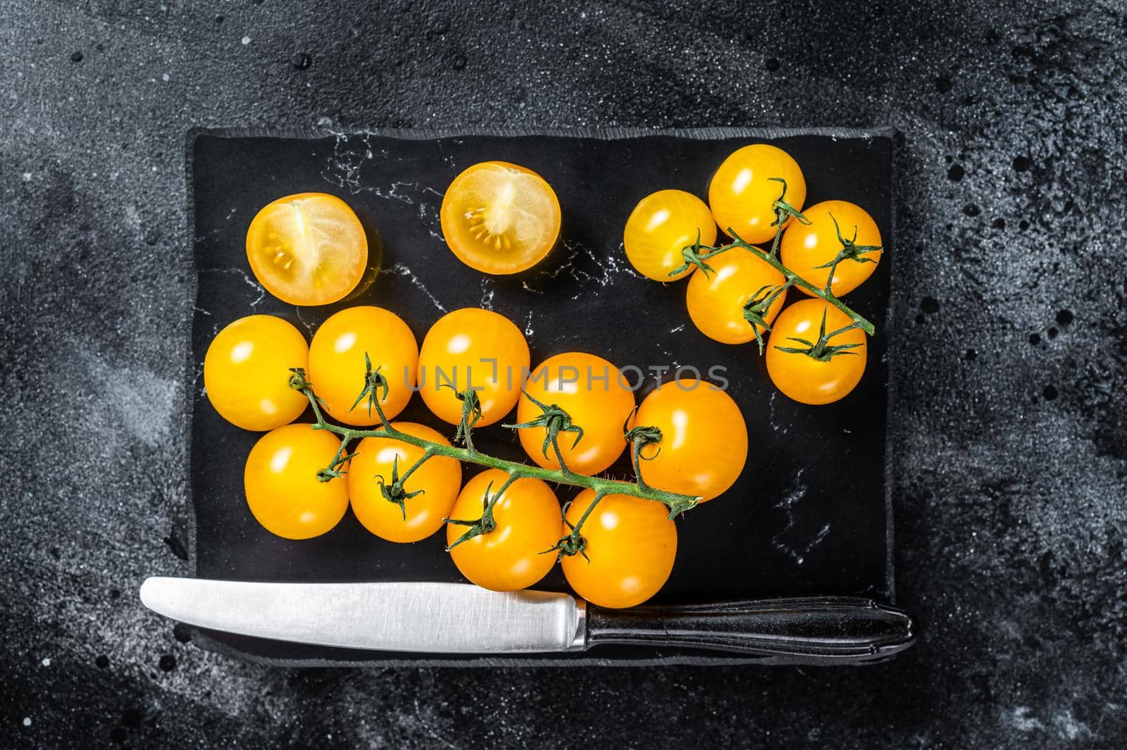 Bunch of yellow cherry tomato on a marble board. Black background. Top view.