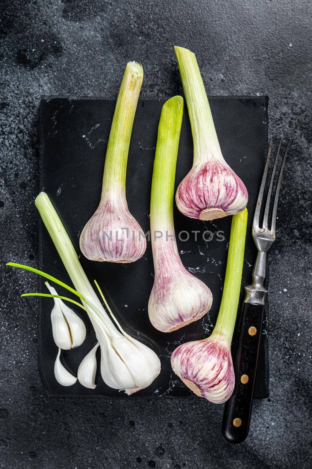 Raw Spring young garlic bulbs and cloves on marble board. Black background. Top view.