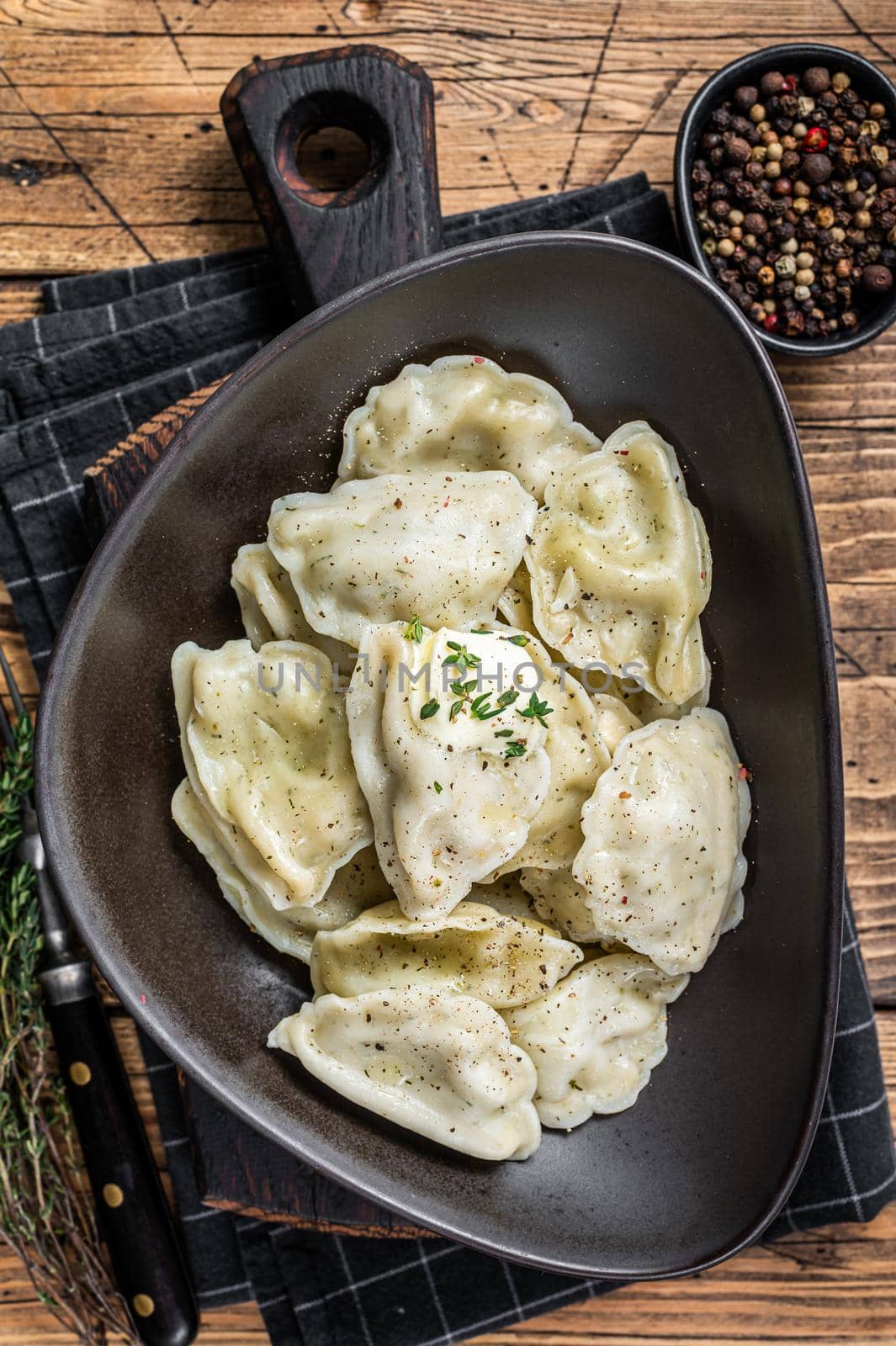 Dumplings pierogi with potato in a plate with herbs and butter. Wooden background. Top View.