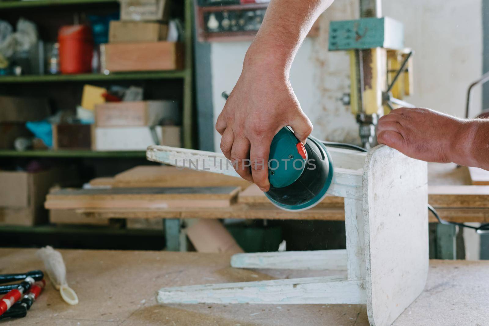 A man is polishing a white old stool. Grinding machine. Restoration of furniture.