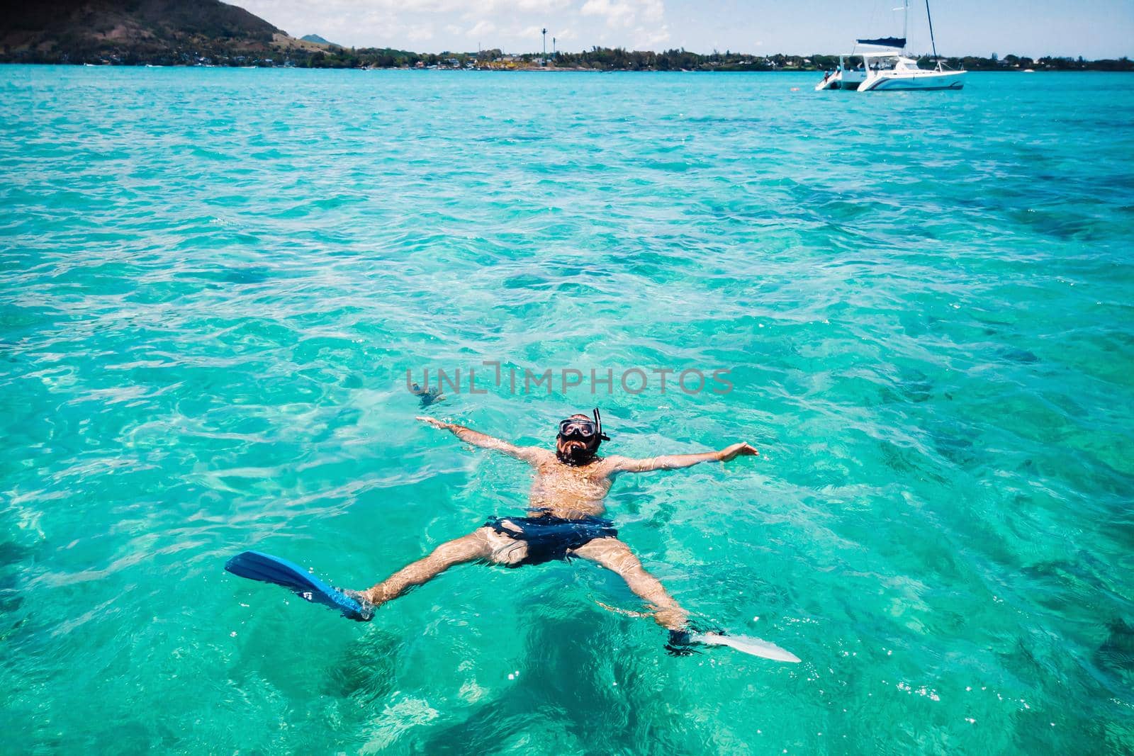A guy in fins and a mask swims in a lagoon on the island of Mauritius by Lobachad