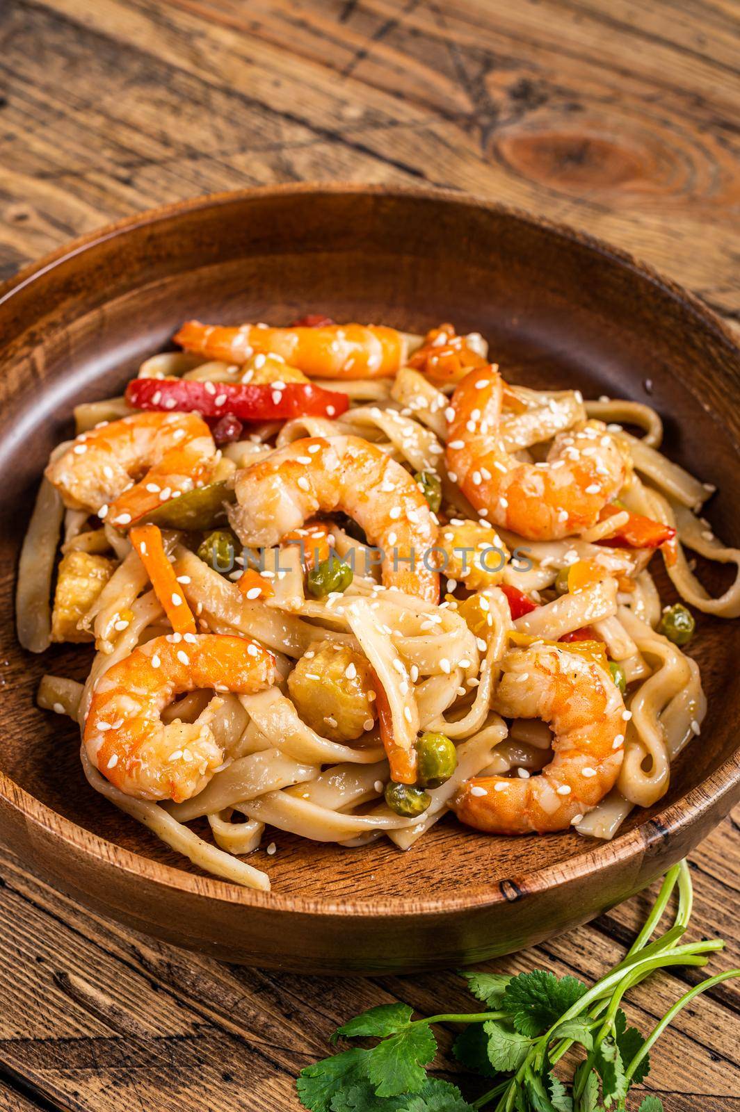 Udon stir-fry noodles with shrimp prawns in a wooden bowl. wooden background. Top view.