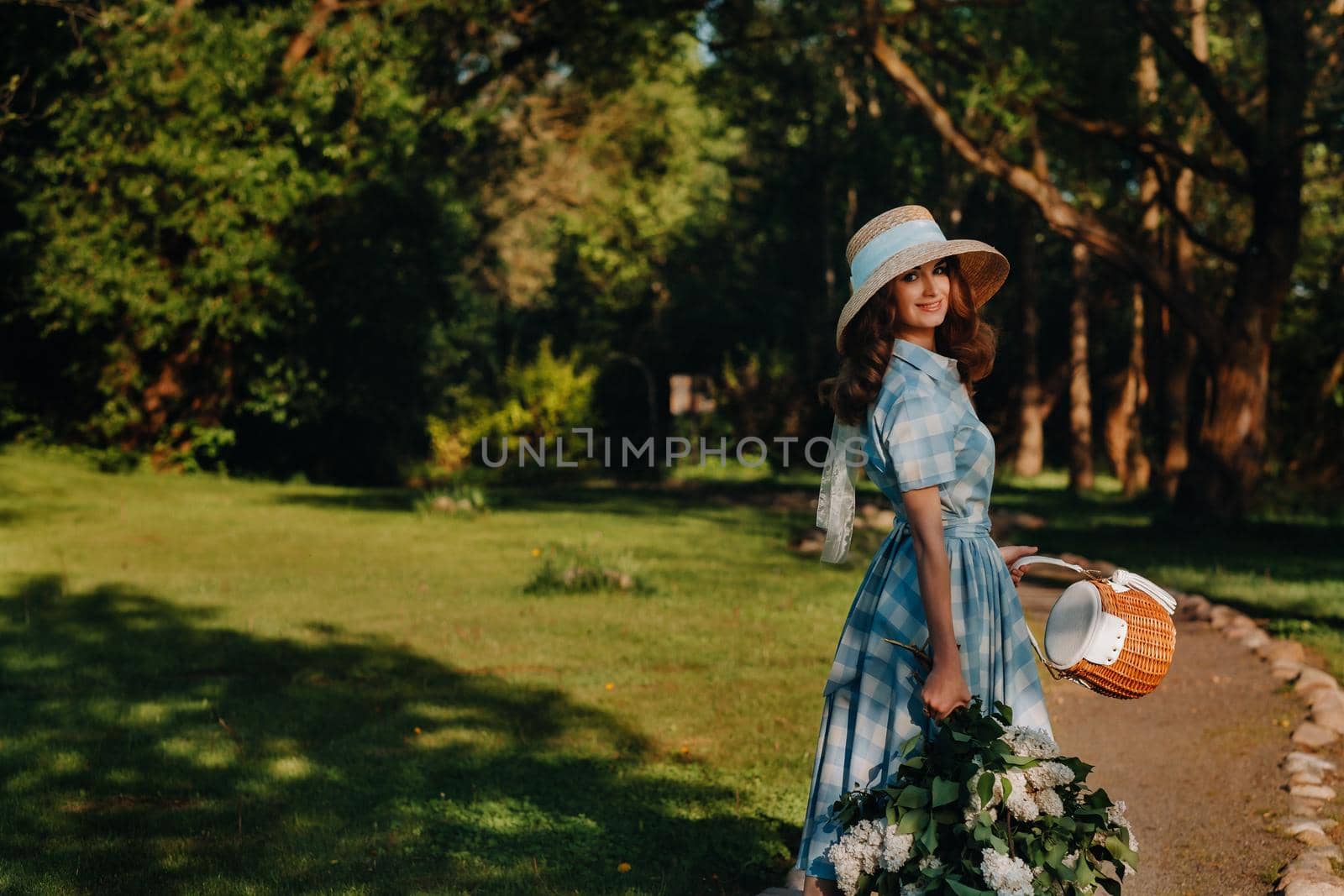 Portrait of a beautiful girl with long hair, a straw hat and a long summer dress with lilac flowers in the garden.