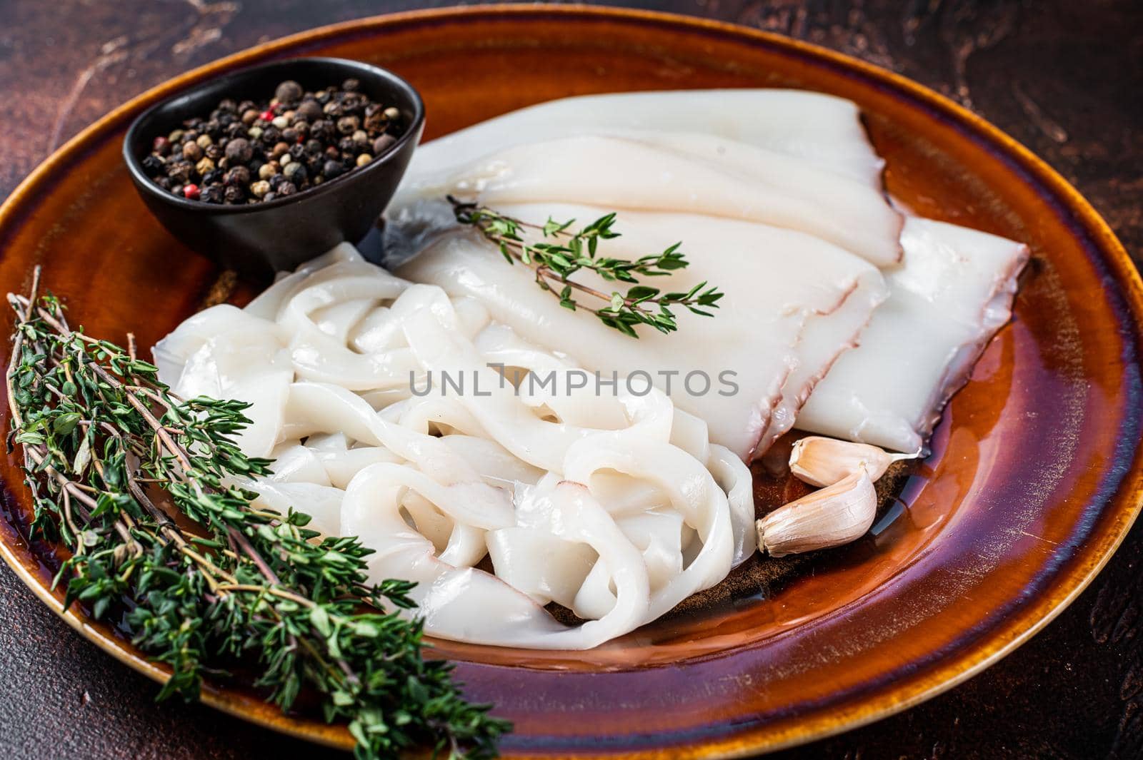 Sliced raw rings Calamari in a rustic plate with rosemary. Dark background. Top view.