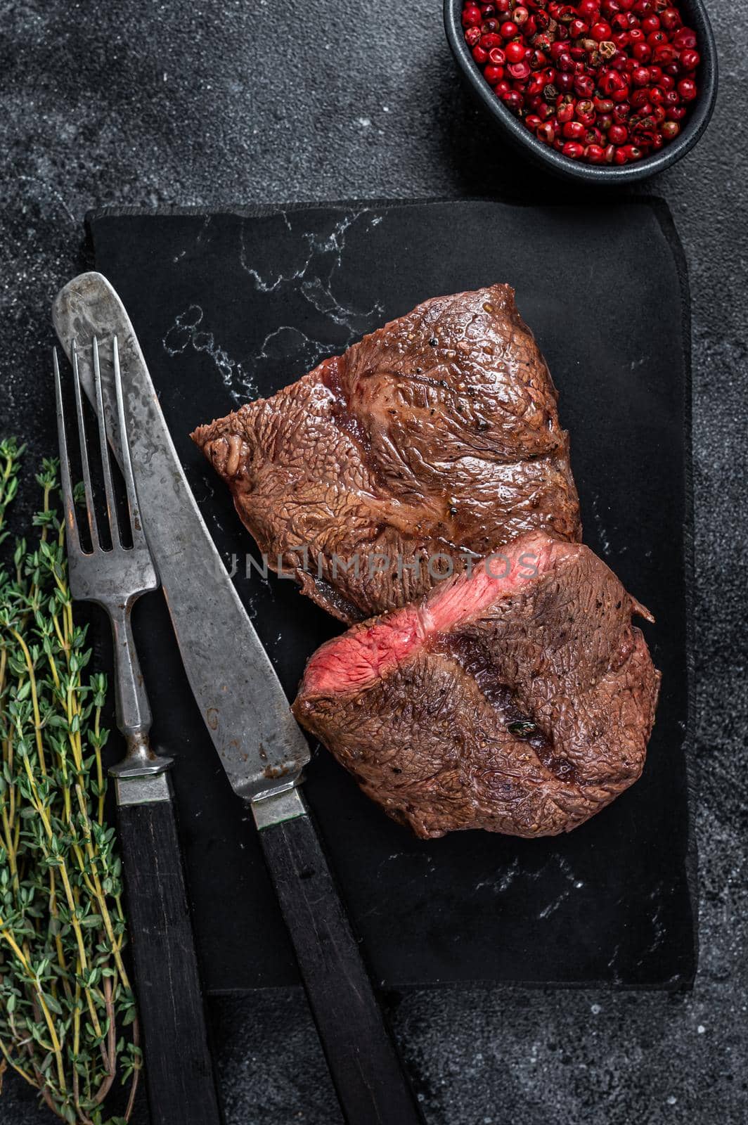 Grilled Top Blade or flat iron roast beef meat steaks on marble board. Black background. Top View.