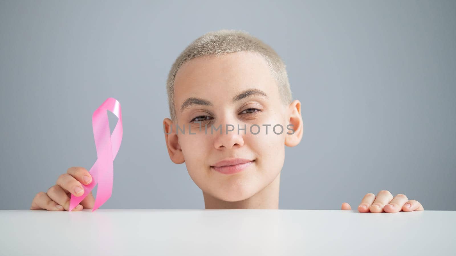 Young woman with short hair wearing a white t-shirt holding a pink ribbon as a symbol of breast cancer on a white background. by mrwed54