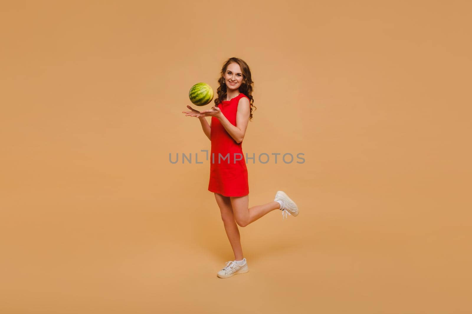 Beautiful girl in a dress throws up a small watermelon.