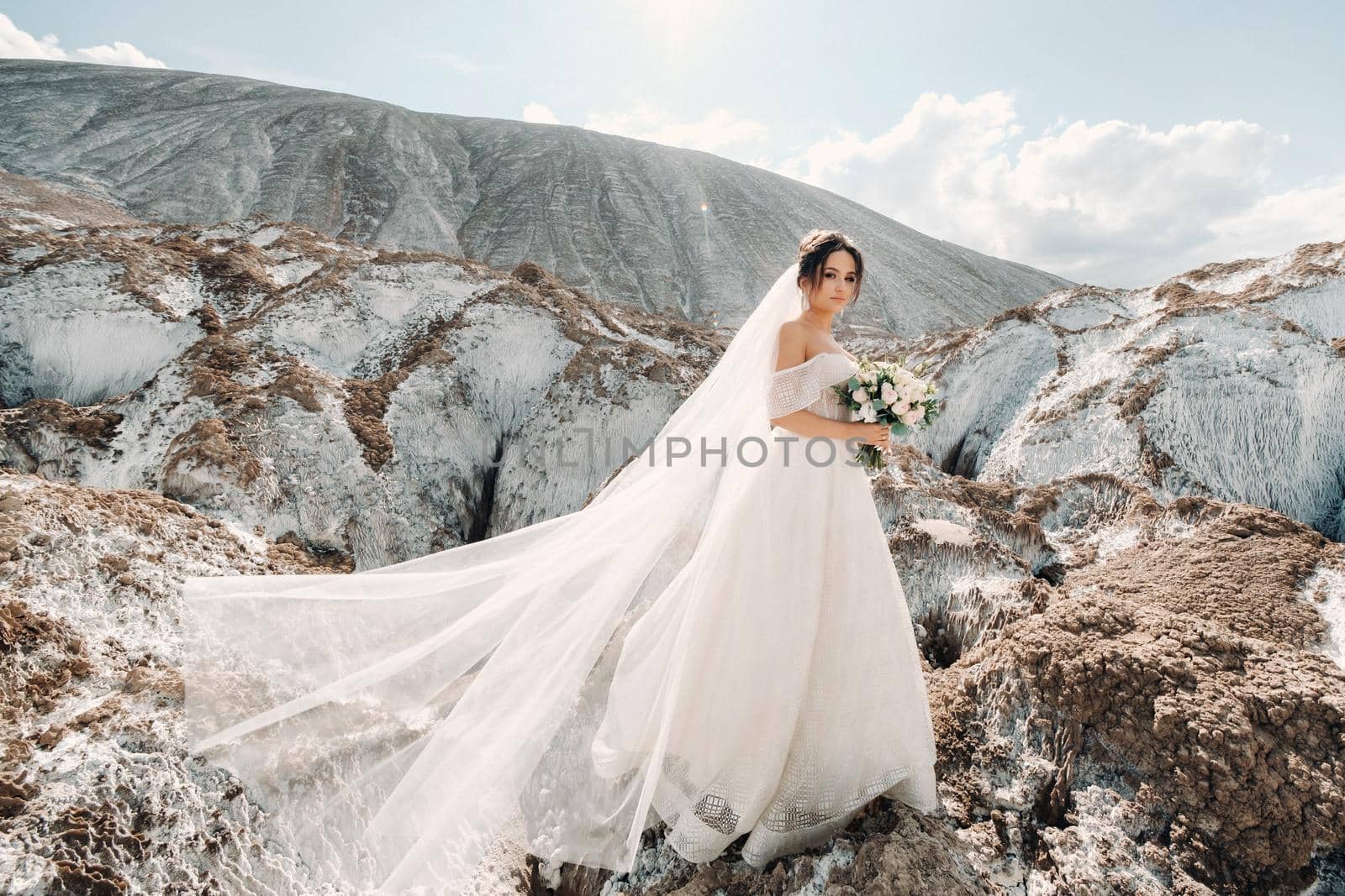 Beautiful bride in a wedding dress with a bouquet on the top of the salt mountains. A stunning young bride with curly hair . Wedding day. . Beautiful portrait of the bride without the groom