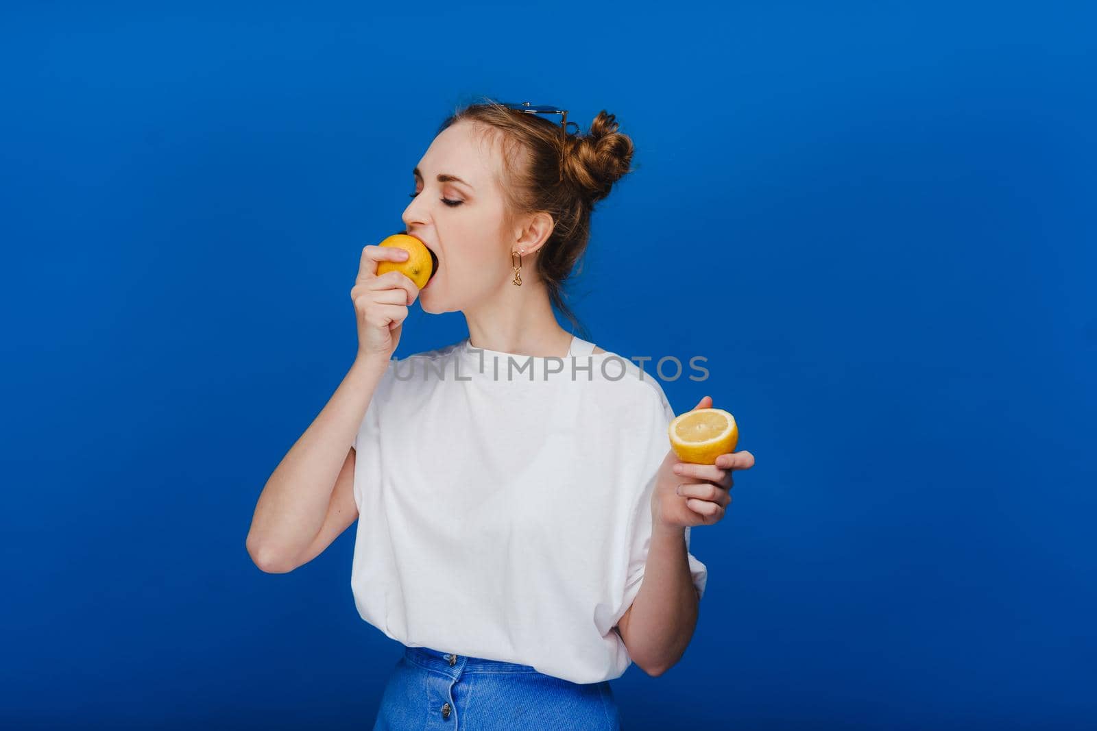 Beautiful brunette woman takes a bite of a lemon. Girl on a blue background.