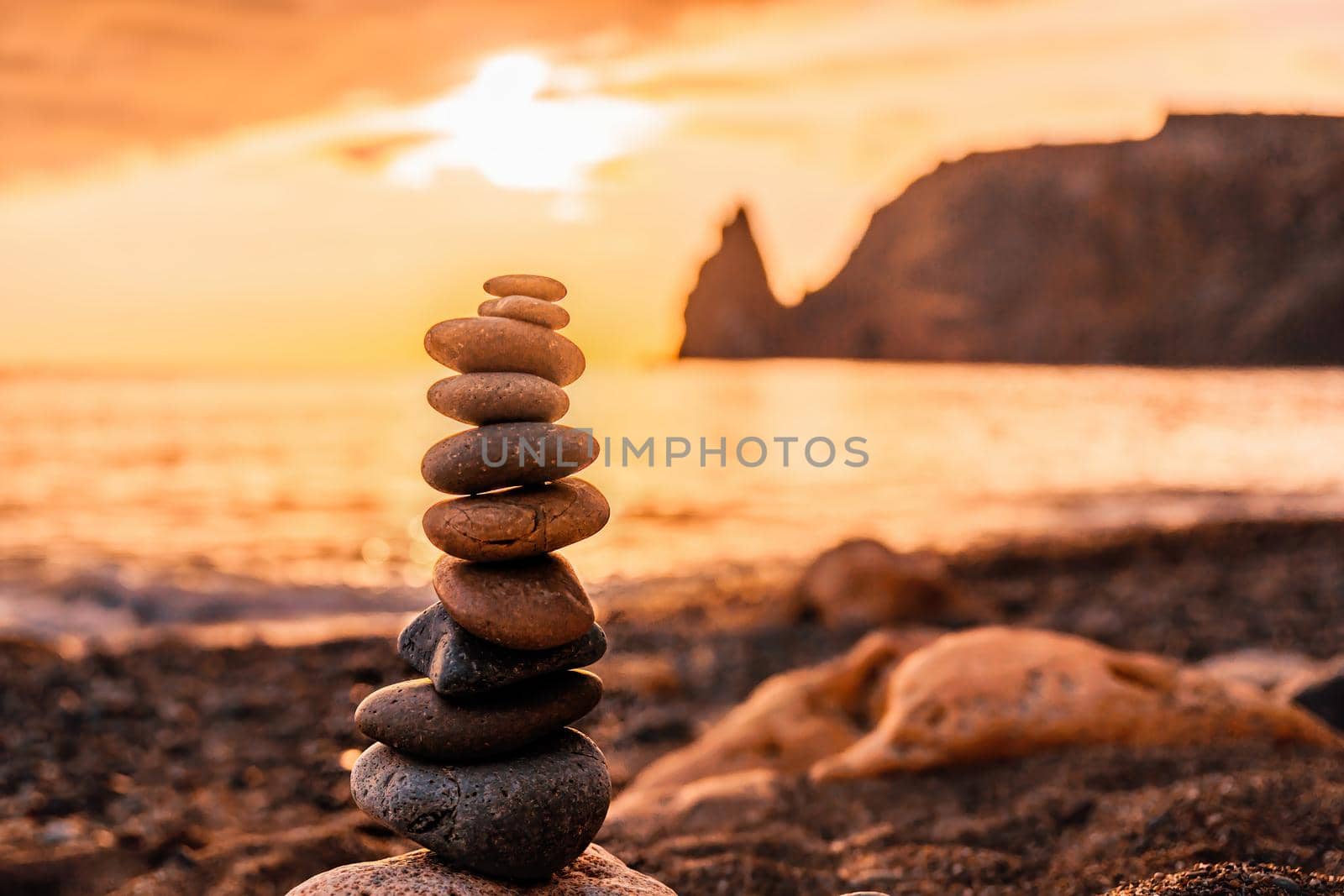 Balanced Pebbles Pyramid on the Beach on Sunny Day and Clear Sky at Sunset. Blue Sea on Background Selective focus, zen stones on sea beach, meditation, spa, harmony, calm, balance concept.