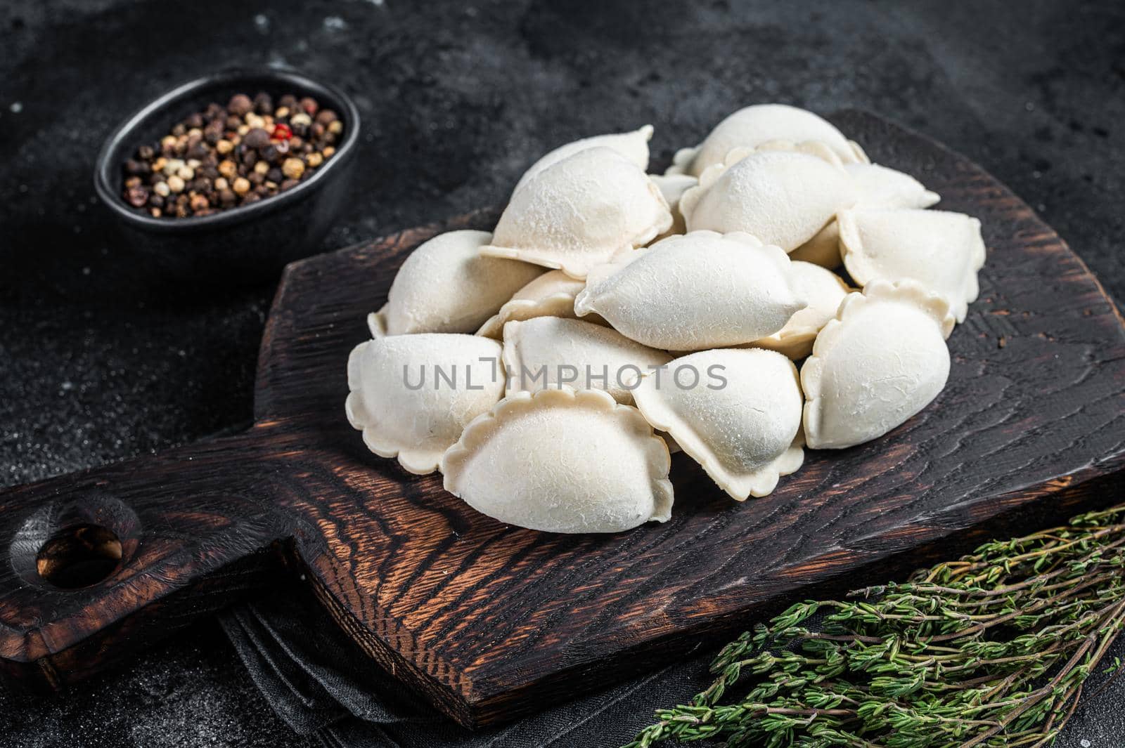 Frozen raw dumplings pierogi with potato on a wooden board. Black background. Top View by Composter