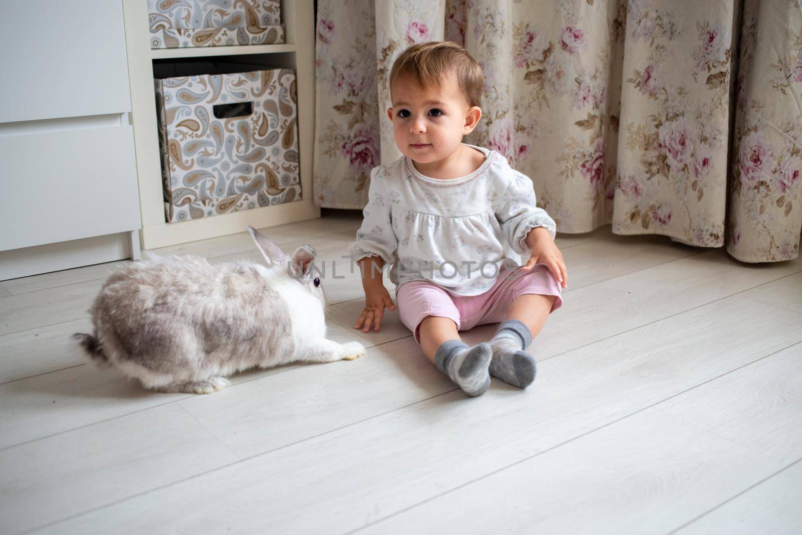 charming baby playing with decorative rabbit at home