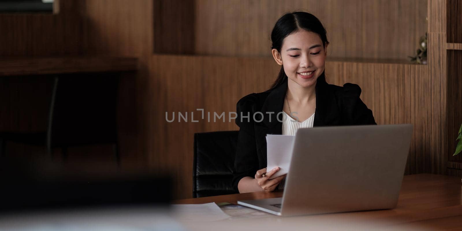 Charming Asian woman working at the office using a laptop. business female checking paperwork with copy space.
