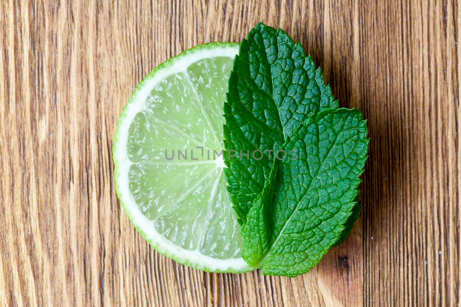 round lime slice and green mint on a wooden table, close-up on top