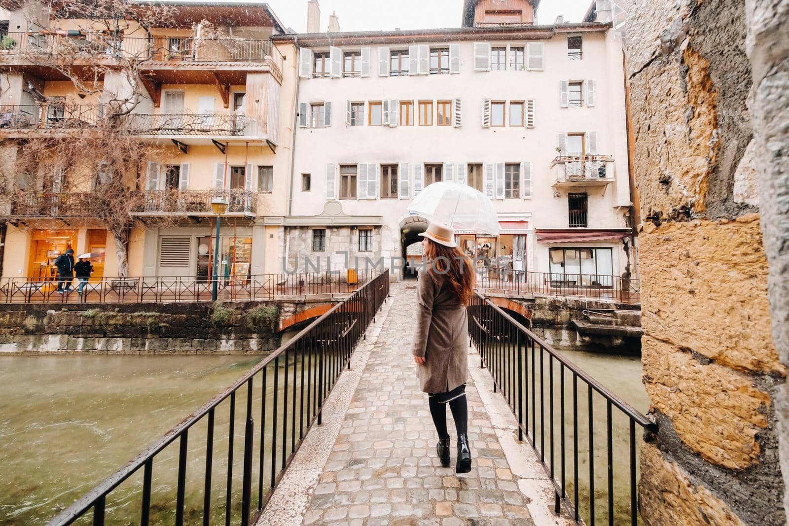beautiful romantic girl in a coat and hat with a transparent umbrella in Annecy. France. The girl in the hat in France.