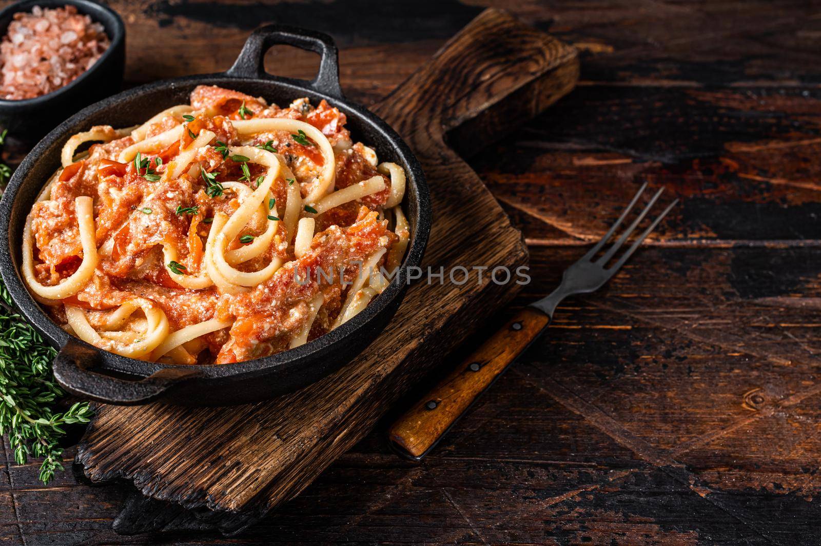 Trendy baked Feta pasta with Oven roasted tomatoes and cheese in a pan. Dark wooden background. Top view. Copy space.