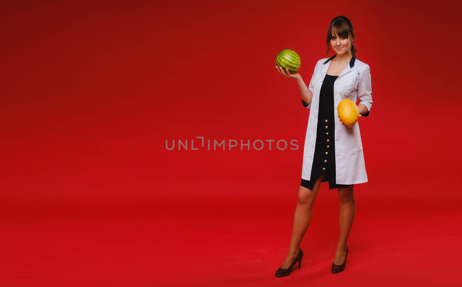 a doctor in a white coat holds fruit watermelon and melon on a red background.