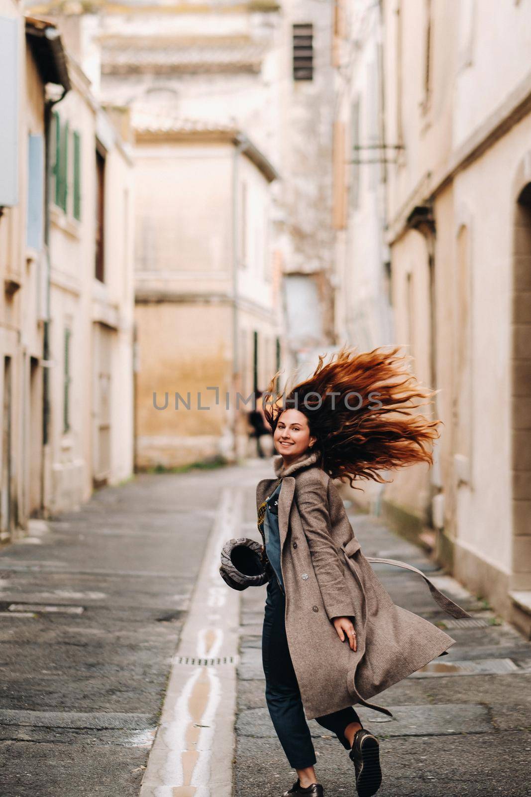 a beautiful romantic girl in a coat with her hair down runs through the old city of Avignon. France. Girl in a coat in France.