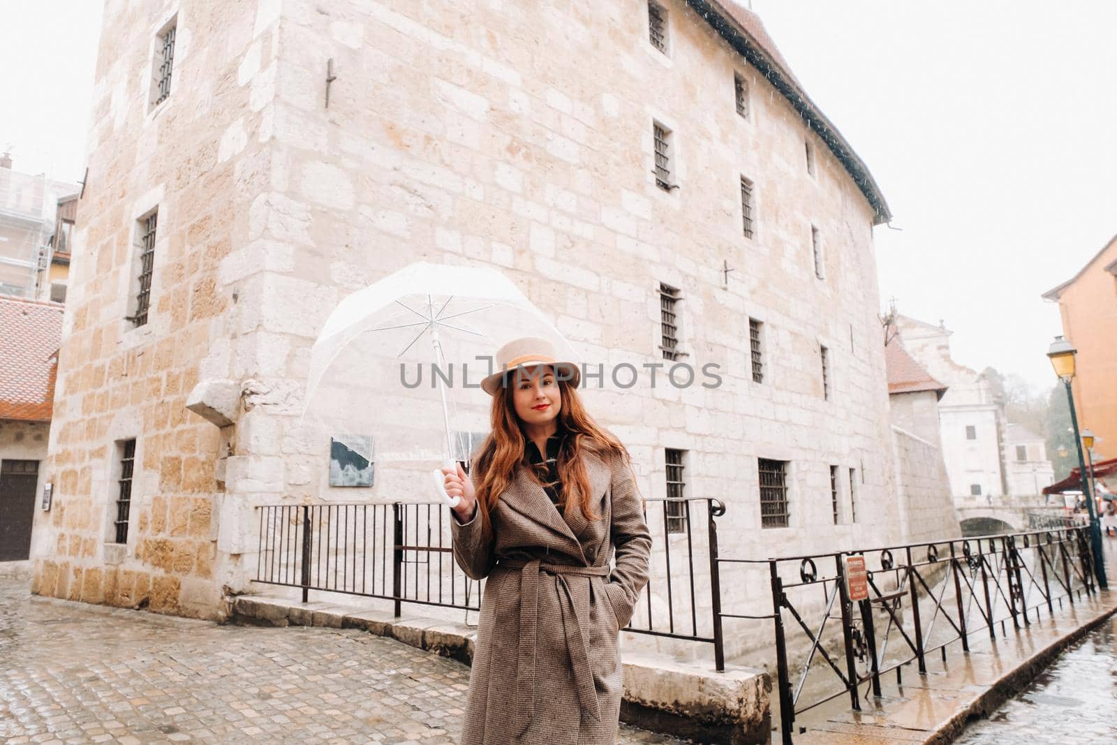 beautiful romantic girl in a coat and hat with a transparent umbrella in Annecy. France. The girl in the hat in France.