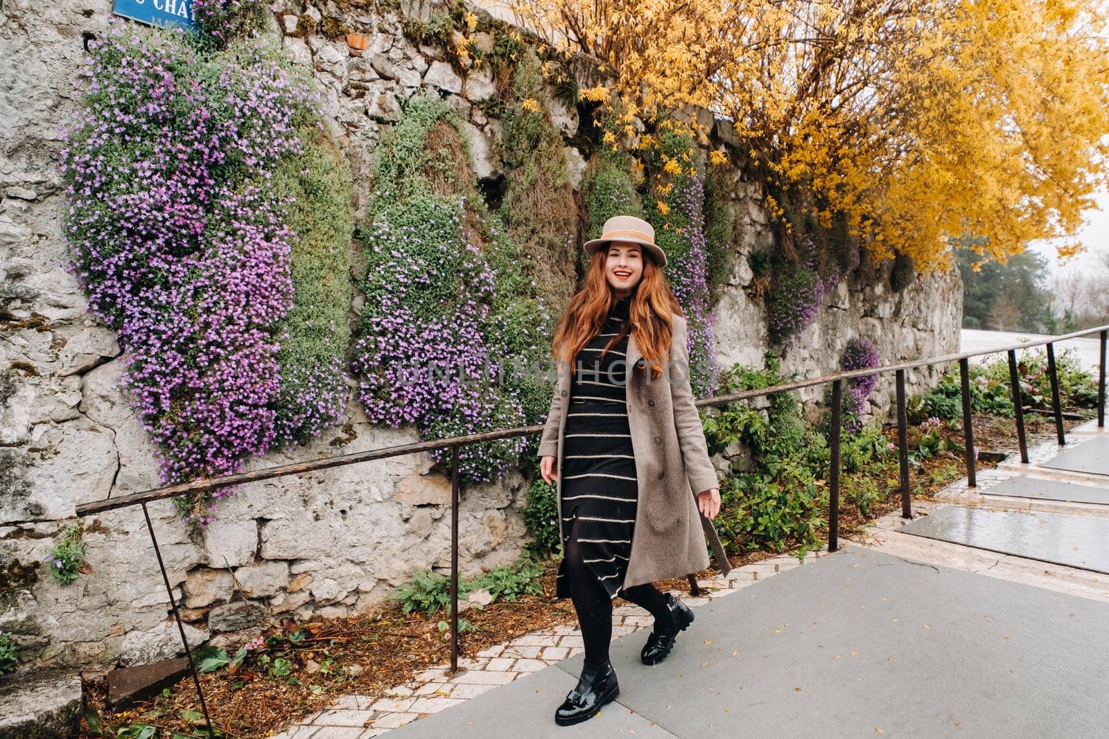 a beautiful romantic girl in a coat and hat walks in Annecy. France. Girl in a hat in France on the background of flowering plants.