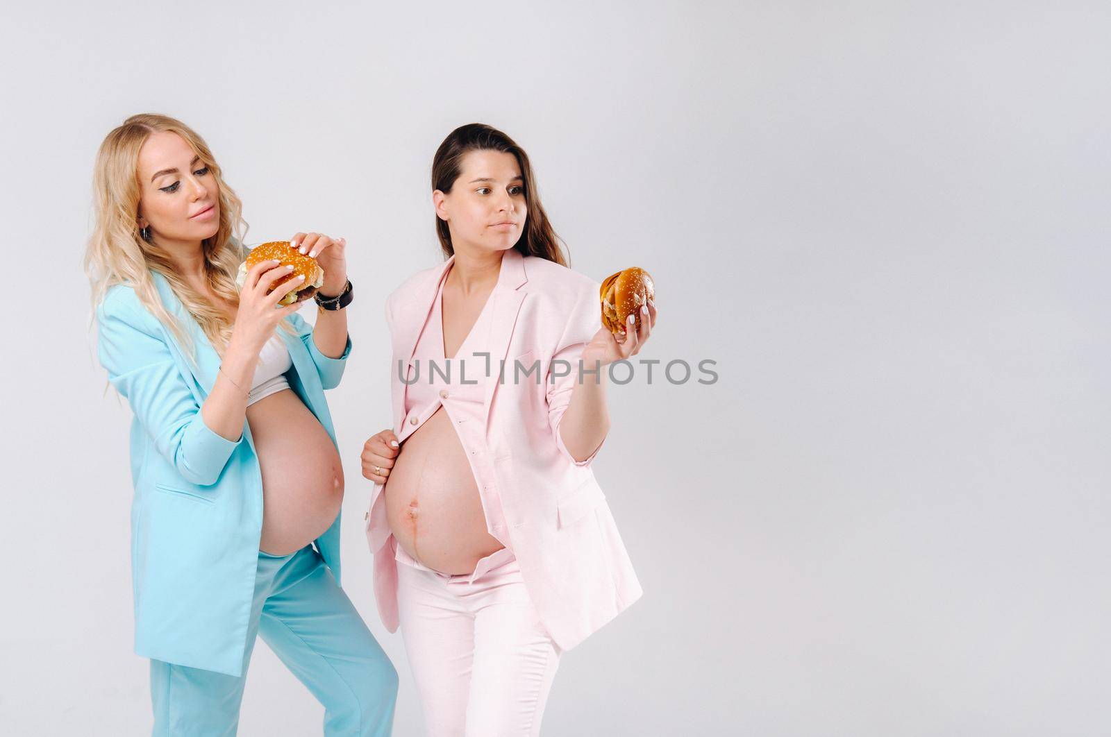 Two pregnant women in suits with hamburgers in their hands on a gray background by Lobachad