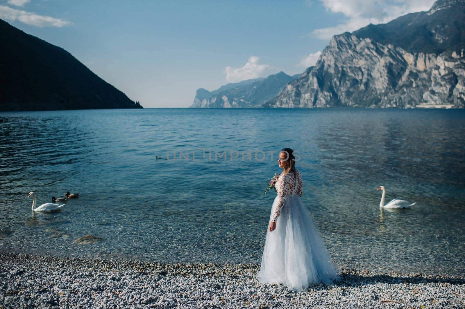 a girl in a smart white dress walks along the embankment of lake Garda.A woman is photographed against the background of a mountain and lake in Italy.Torbole.