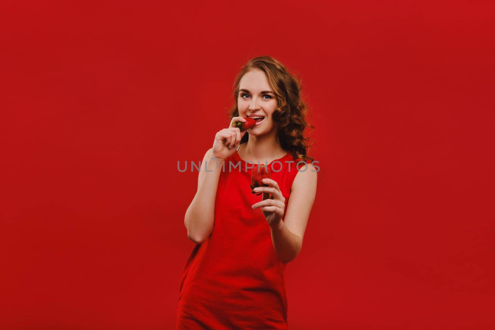 Sweet strawberries. Beautiful bright girl in retro style eating a strawberry. Happy pin up woman isolated on pink wall background eating strawberry