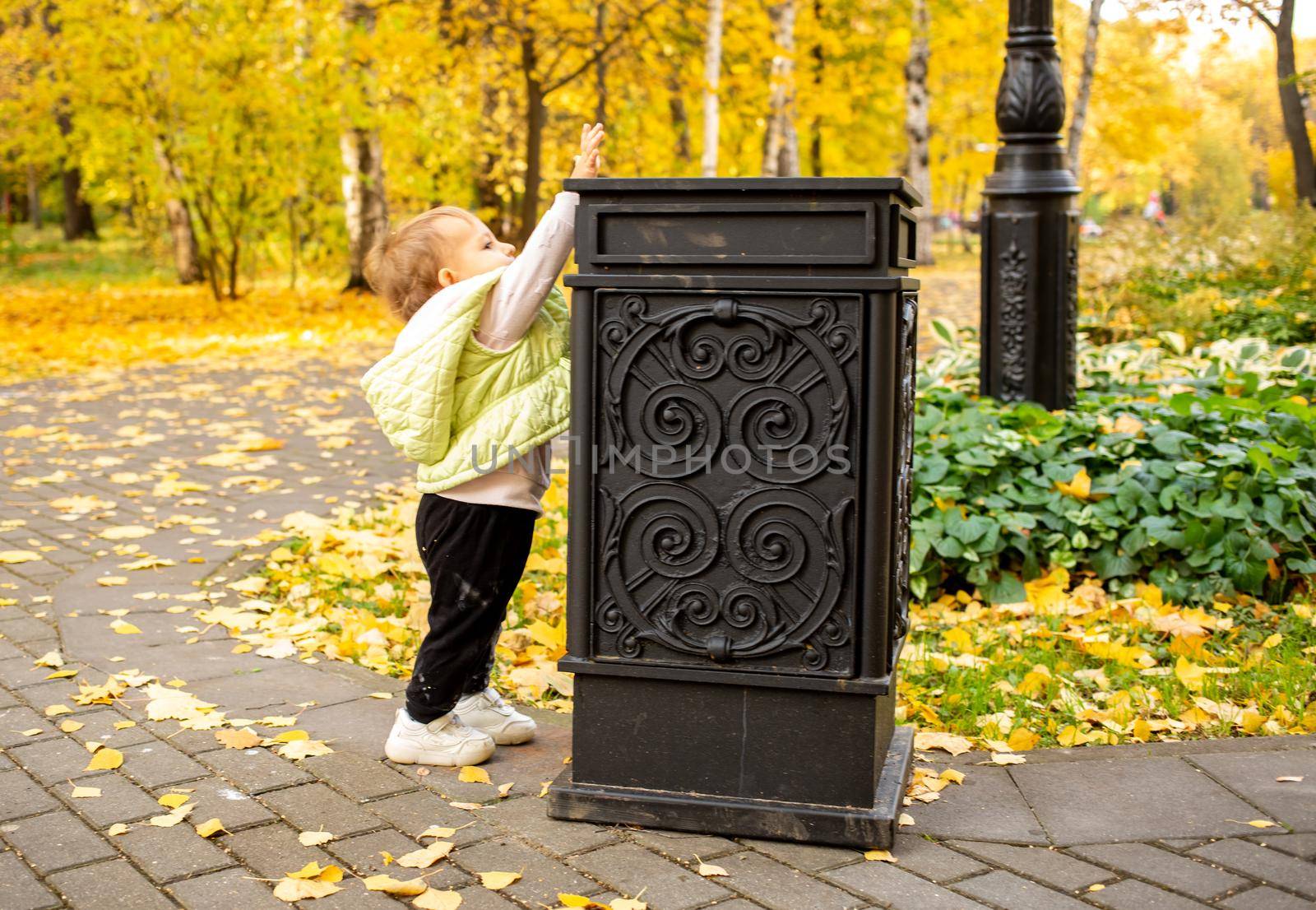 litte toddler throws trash into trash can in autumn park. instilling cultural norms from birth