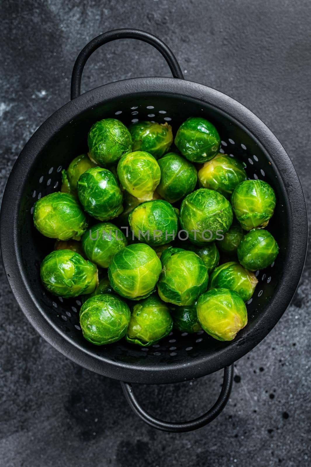 Brussels sprouts green cabbage in colander. Black background. Top view.