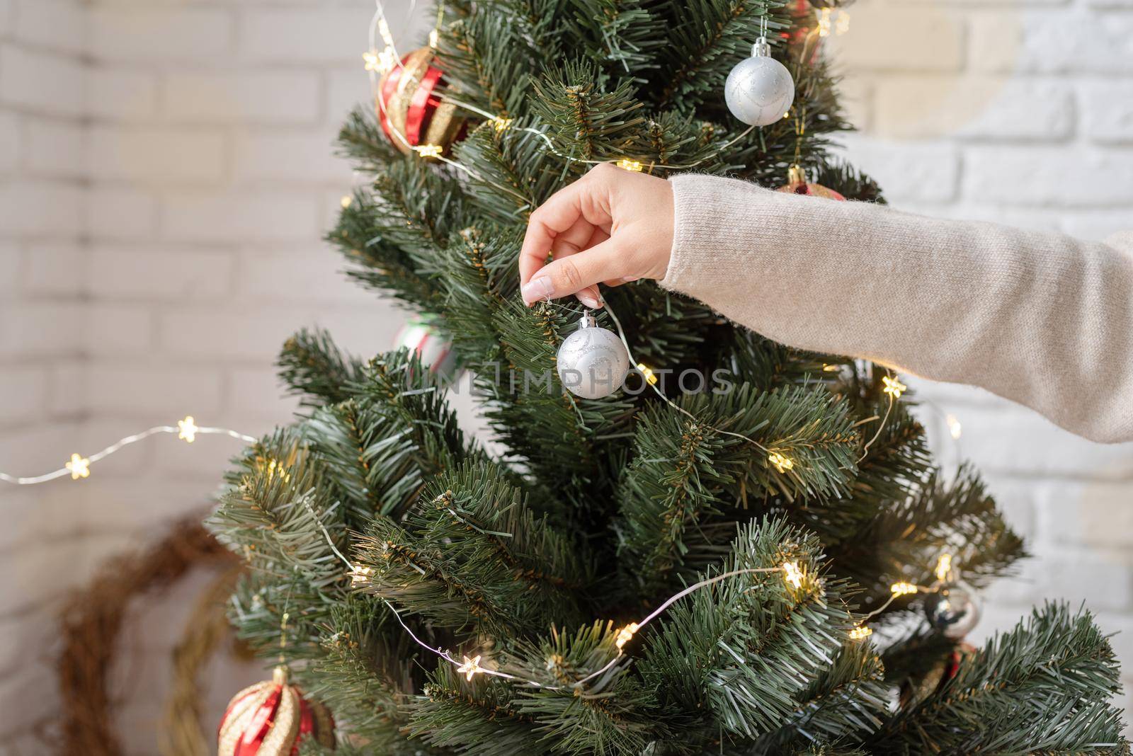 woman hand decorating the Christmas tree with fairy lights by Desperada