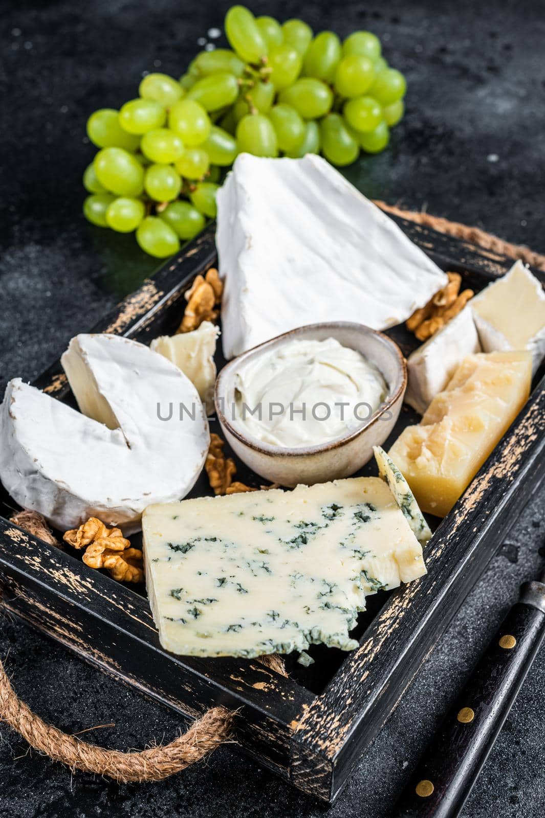 Assorted Cheese platter with Brie, Camembert, Roquefort, parmesan, blue cream cheese, grape and nuts. Black background. Top view by Composter