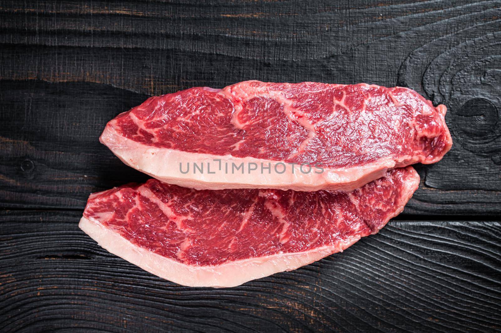 Raw rump steak or top sirloin cap beef meat steaks on butcher table. Black wooden background. Top view.