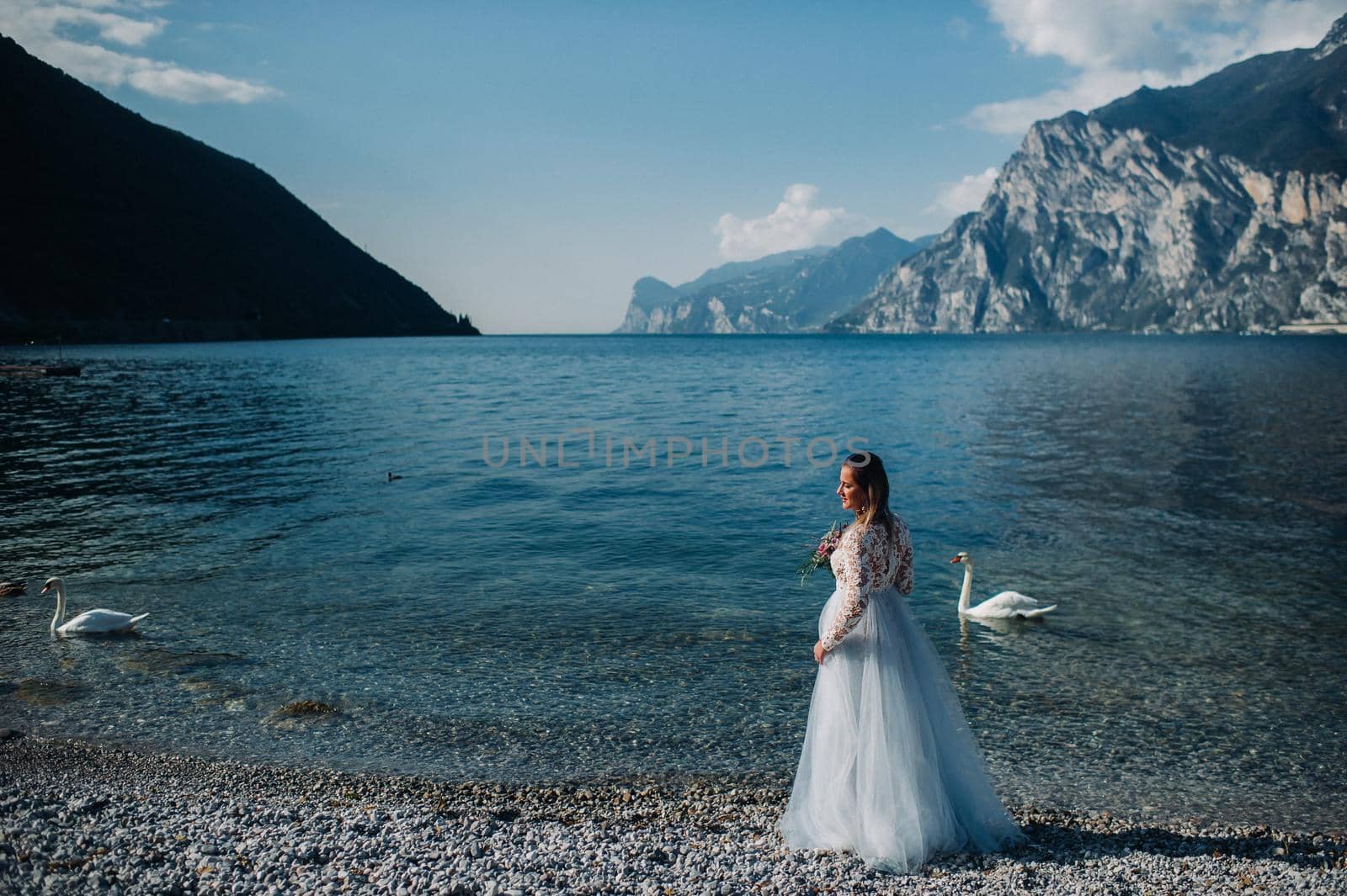 a girl in a smart white dress walks along the embankment of lake Garda.A woman is photographed against the background of a mountain and lake in Italy.Torbole.